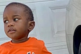 A young black boy wearing an orange T-shirt.