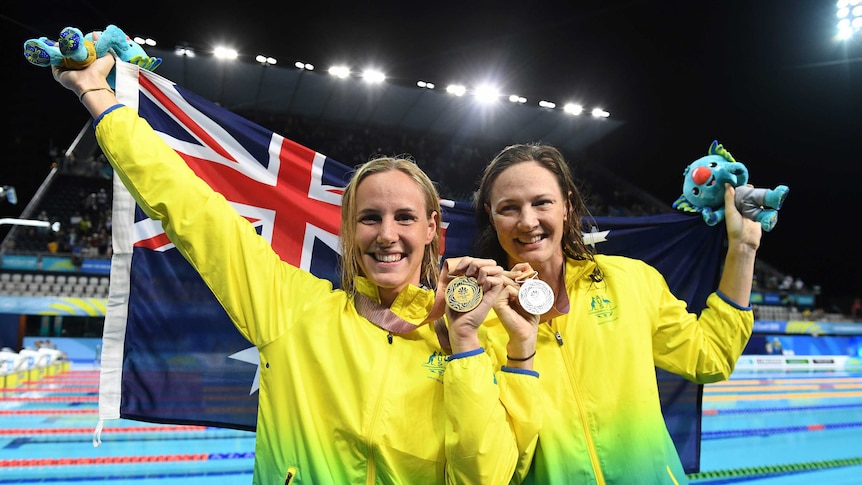 Bronte Campbell and Cate Campbell hold their gold and silver medals, while raising an Australian flag behind them
