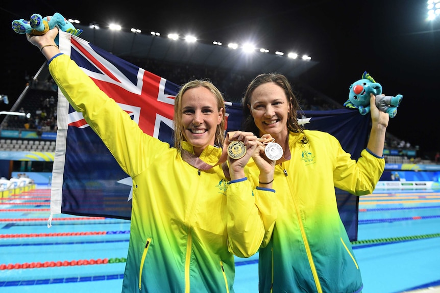 Bronte Campbell and Cate Campbell hold their gold and silver medals, while raising an Australian flag behind them