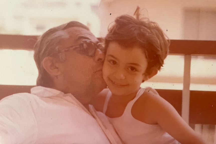 A father kisses his young daughter on the cheek in an old family photo.