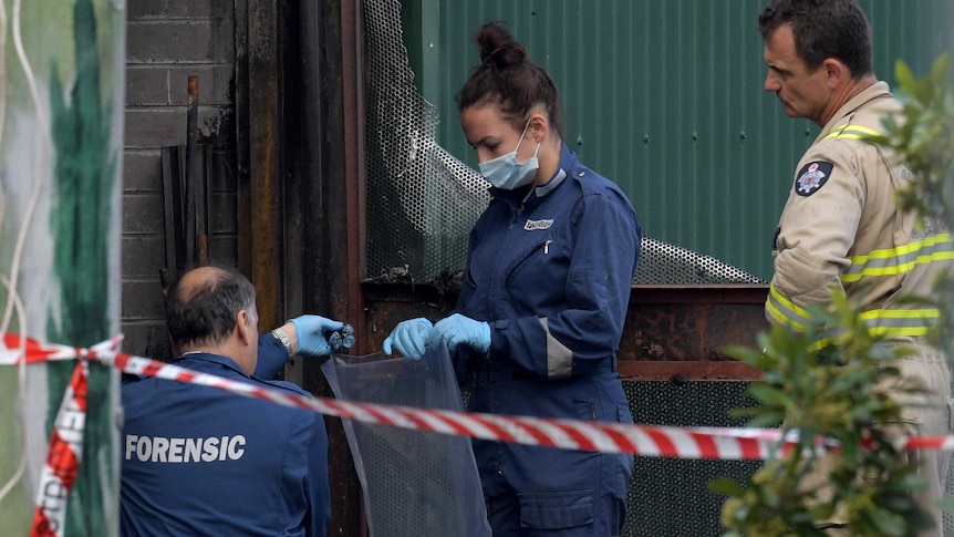 Forensic officers wearing masks place items in a plastic bag outside a Footscray factory.