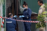 Forensic officers wearing masks place items in a plastic bag outside a Footscray factory.