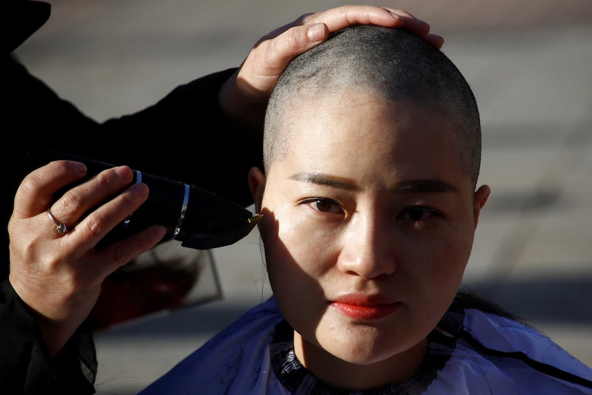 A hand holding a hair clipper shaves the head of Li Wenzu, partner of prominent Chinese rights lawyer Wang Quanzhang.
