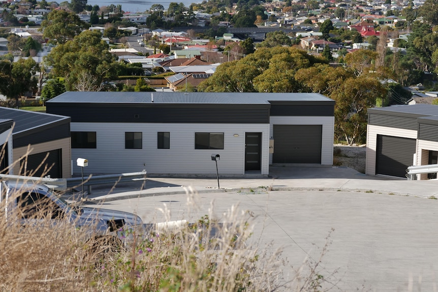 A white rectangular house with a dark grey roof looks over the suburb from a cul de sac 
