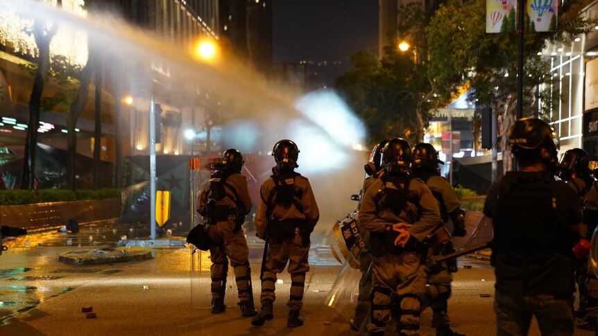 From behind a police cordon, you view them watch on as a water cannon fires on protesters down a street.