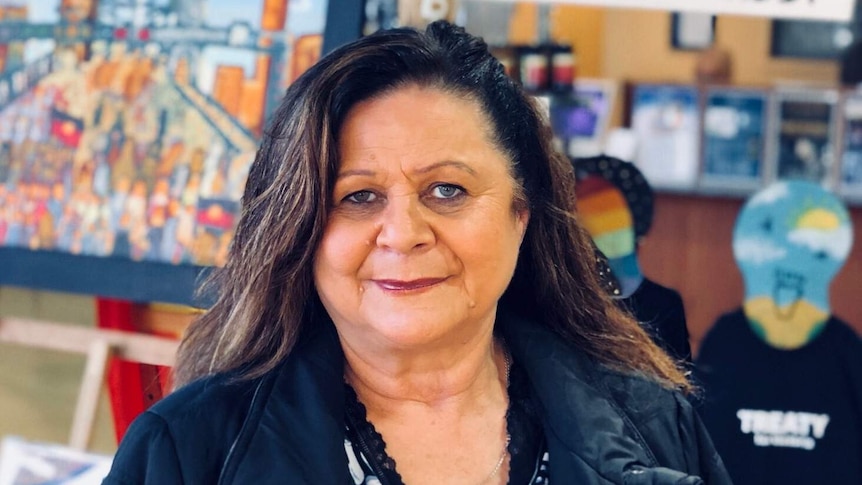 A smiling woman sits in front of some artwork.