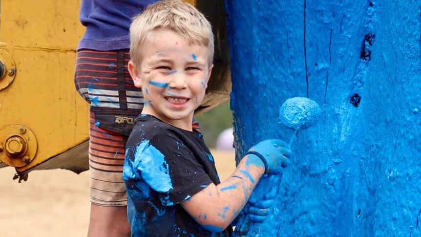 Little boy covered in blue paint painting a tree