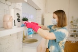 Woman wearing mask and pink gloves cleans her home, in a story about how to clean mould after rain.