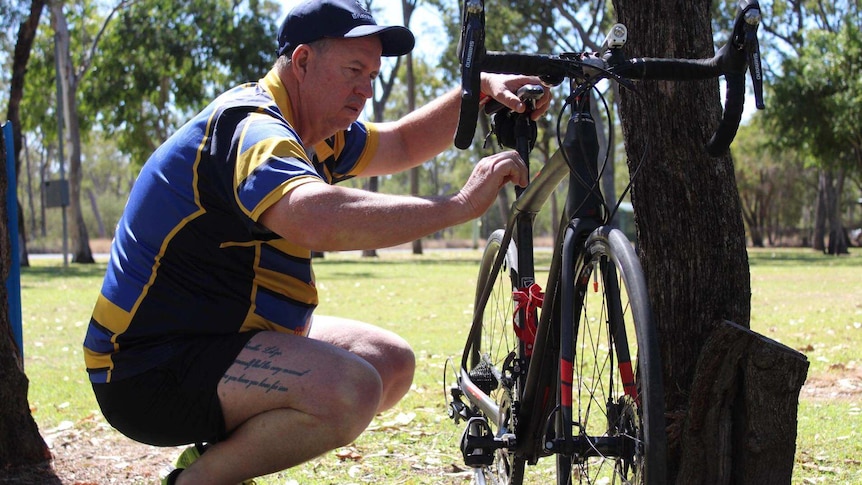 A man looks at a racing bike surrounded by trees