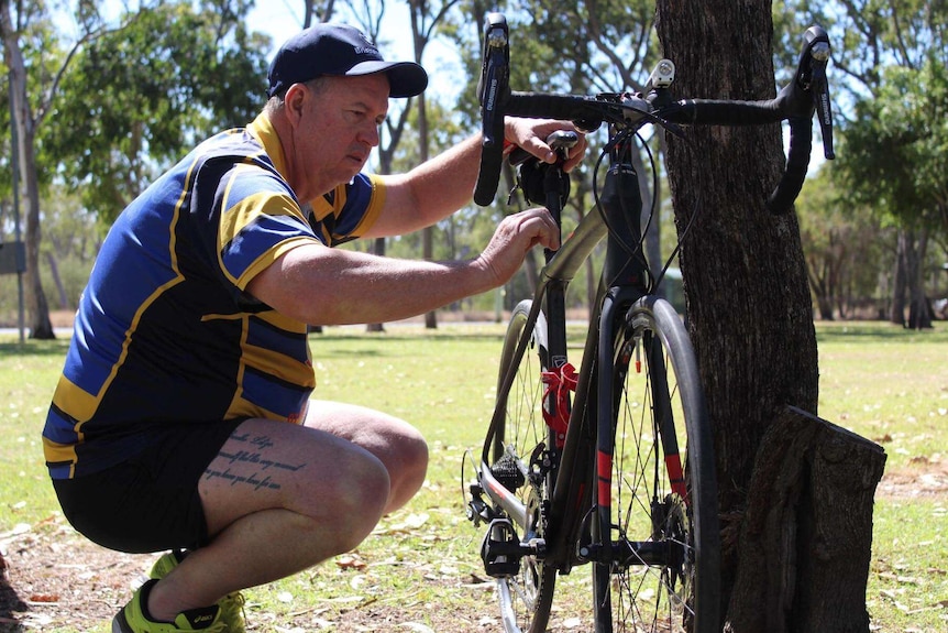 A man looks at a racing bike surrounded by trees