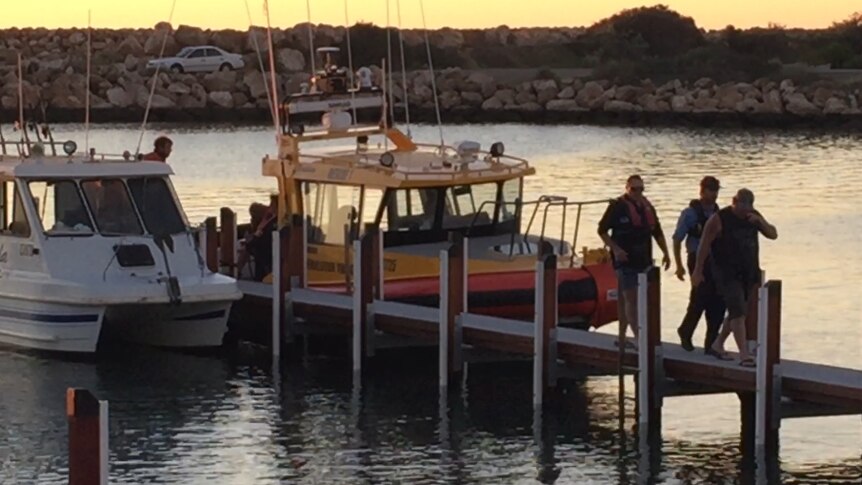 Three men walk along the marina jetty with two boats behind.