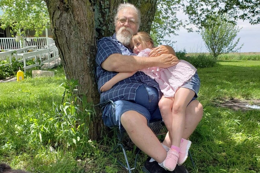 Mike Wolfe sits below a tree holding a young girl in his arms