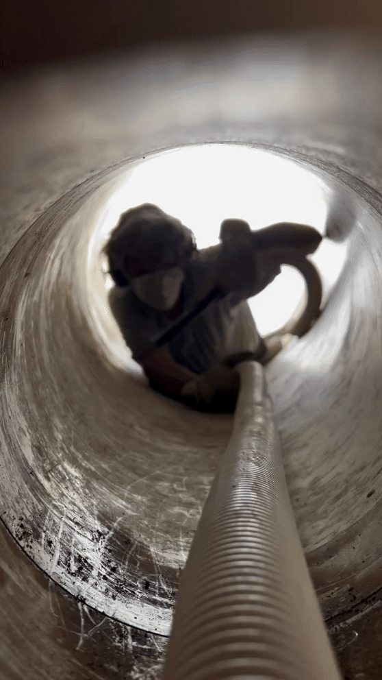 A cleaner in a face mask vacuums the inside of a narrow tunnel.