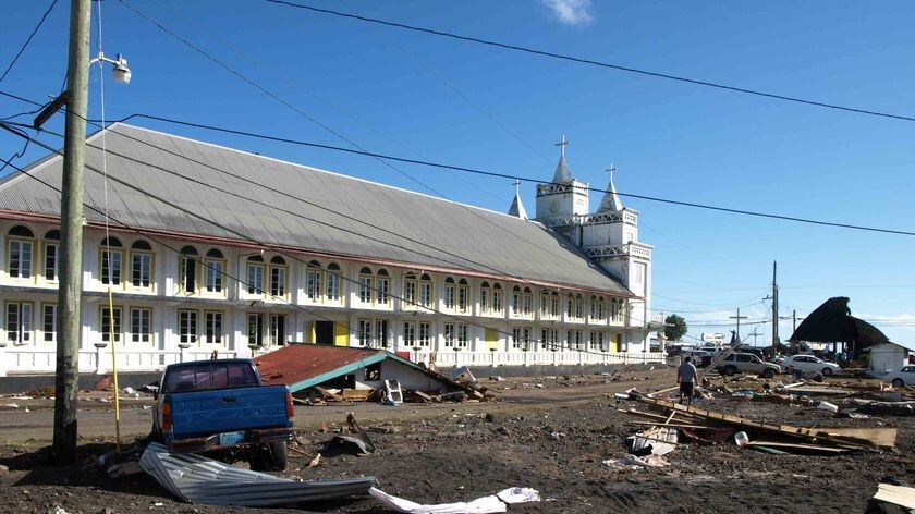 Battered cars and debris are strewn across the ground in front of a church