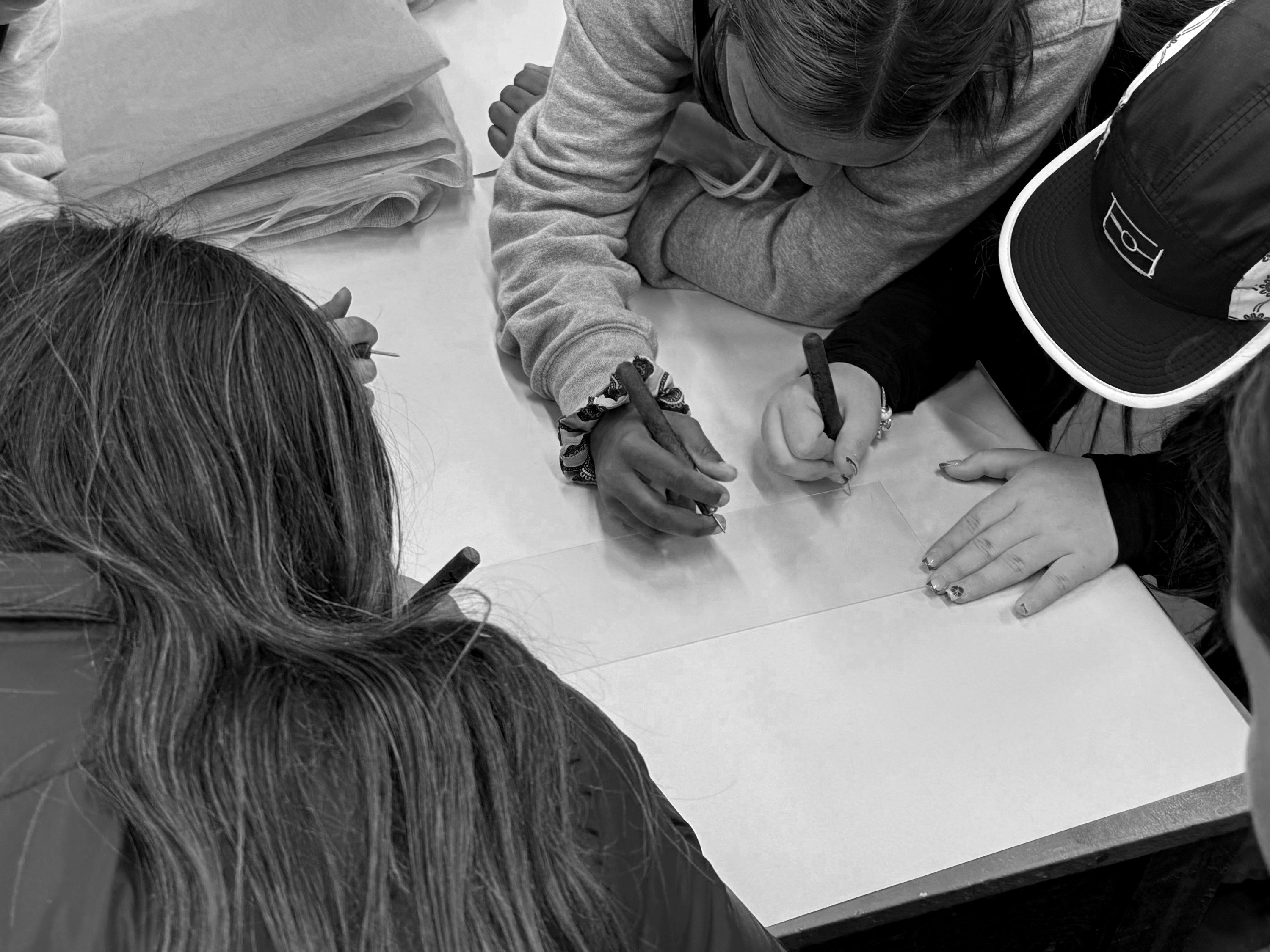 Uma fotografia em preto e branco olhando para três jovens indígenas gravando uma obra de arte.