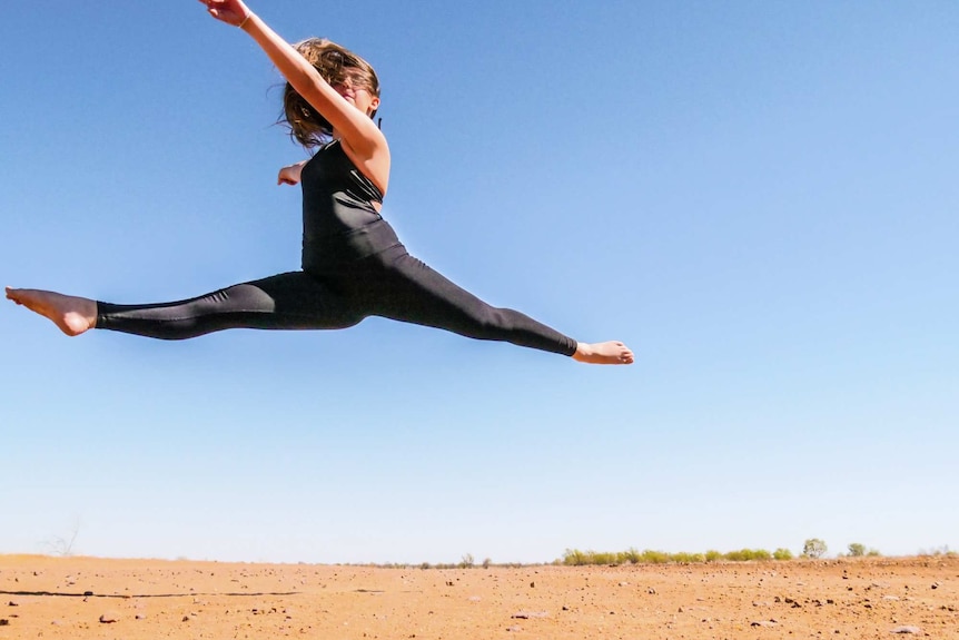 A teenager dancer leaps over the red dirt in Longreach.