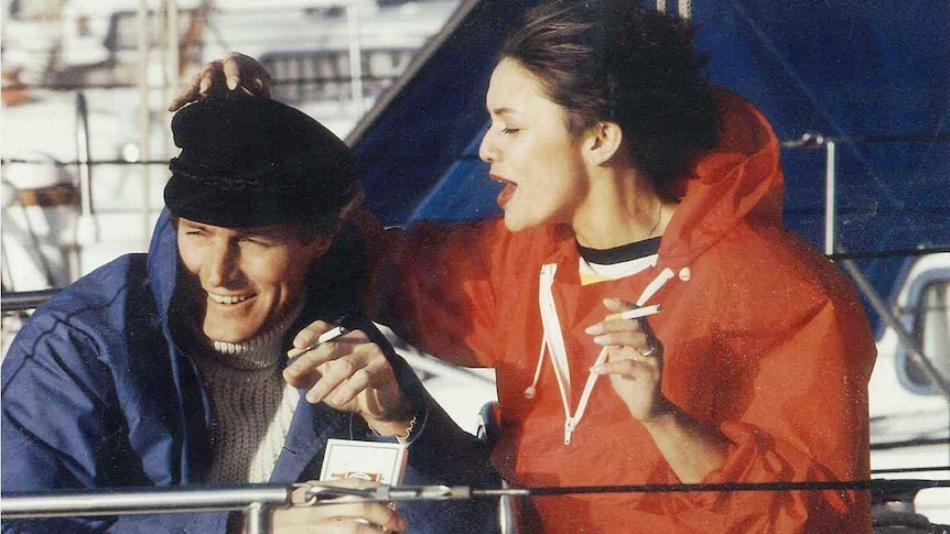 A woman and a man smoke cigarettes on a yacht.