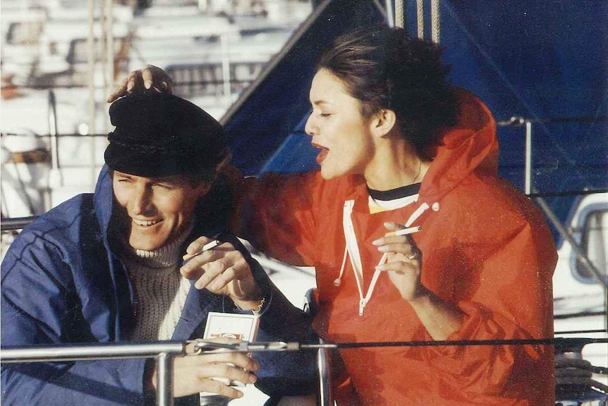 A woman and a man smoke cigarettes on a yacht.