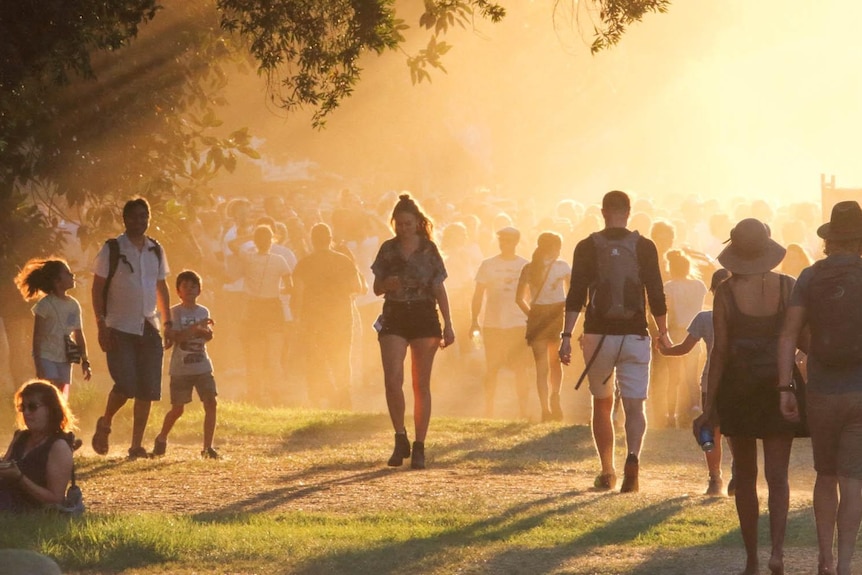 People mill about at a festival with dust hanging in the air.