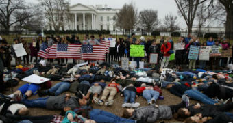 With the White House behind them, people lie pretending to be dead, others stand holding placards and American flags.