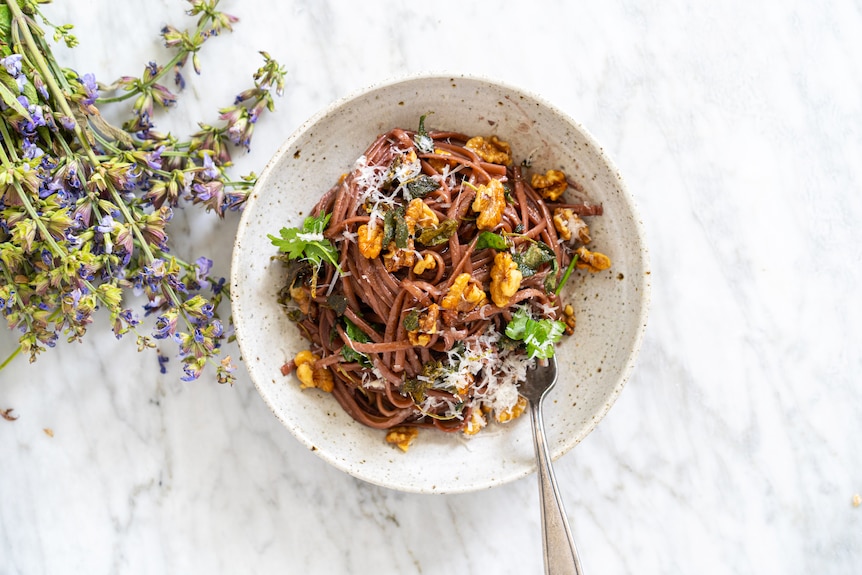 A bowl of red wine pasta topped with grated pecorino, sage, walnuts, an easy vegetarian dinner.