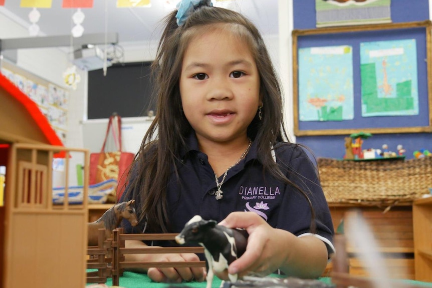 A female pre-primary student poses for a photo in class while playing with toy farm animals.