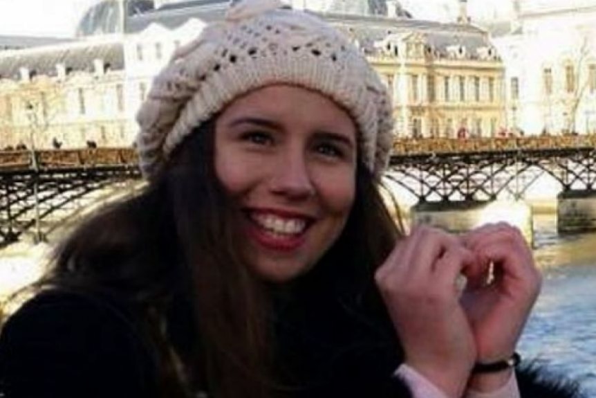 A smiling Masa wearing a white beanie with a European scene behind her.