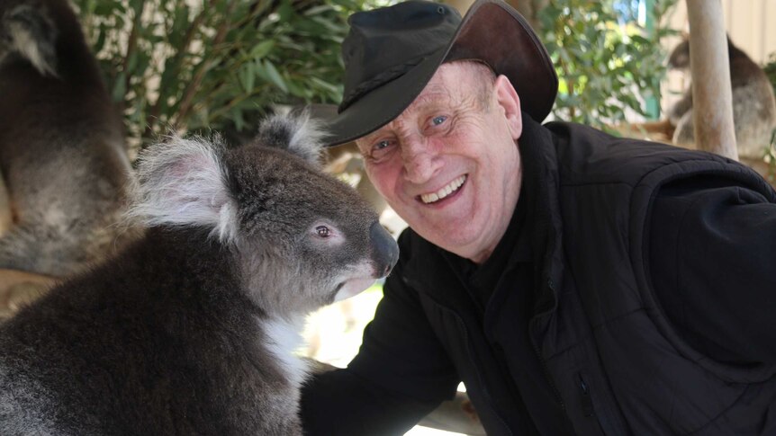 David smiles with a koala in their enclosure.