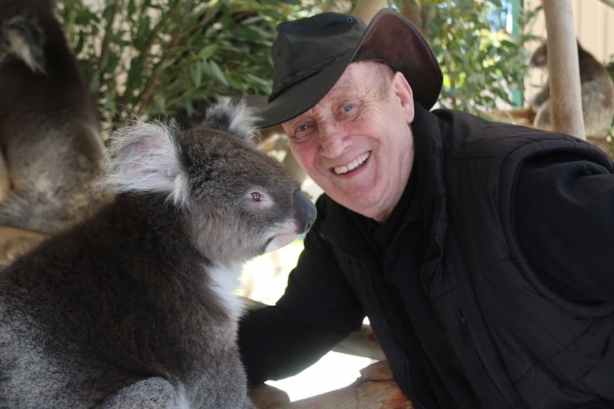 David smiles with a koala in their enclosure.