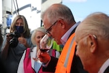 A man smells a glass of wine as people stand around watching him