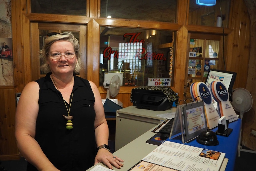 A woman stands behind a counter smiling, with brochures, medals and maps on the counter.