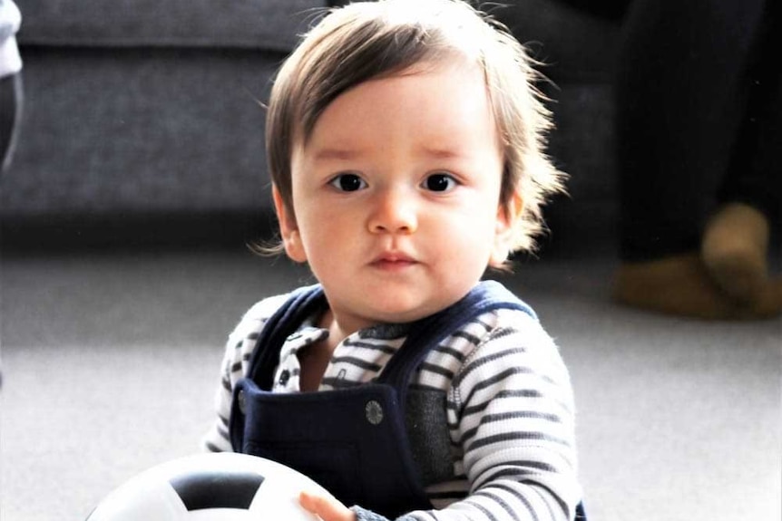 A baby siting up holding a ball.