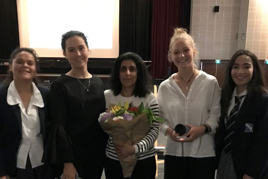 Four young women stand with a teacher holding flowers