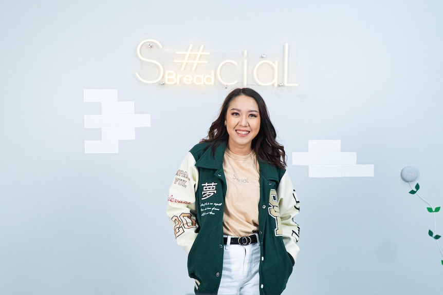 Woman with long hair standing in front of Social Bread's logo.