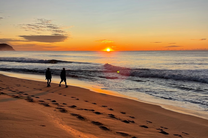 Two people walk in front of sun rise over ocean
