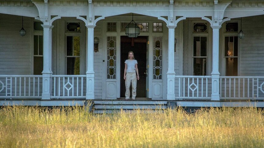 Still image from 2017 film Mother! of lead actress Jennifer Lawrence standing on the porch of a white house.