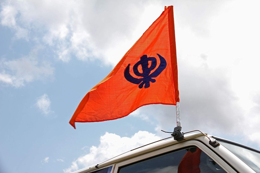 A bright orange flag depicting a Sikh Khanda attached to the top of a van.