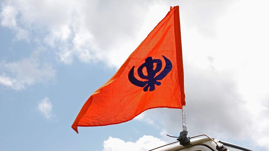 A bright orange flag depicting a Sikh Khanda attached to the top of a van.