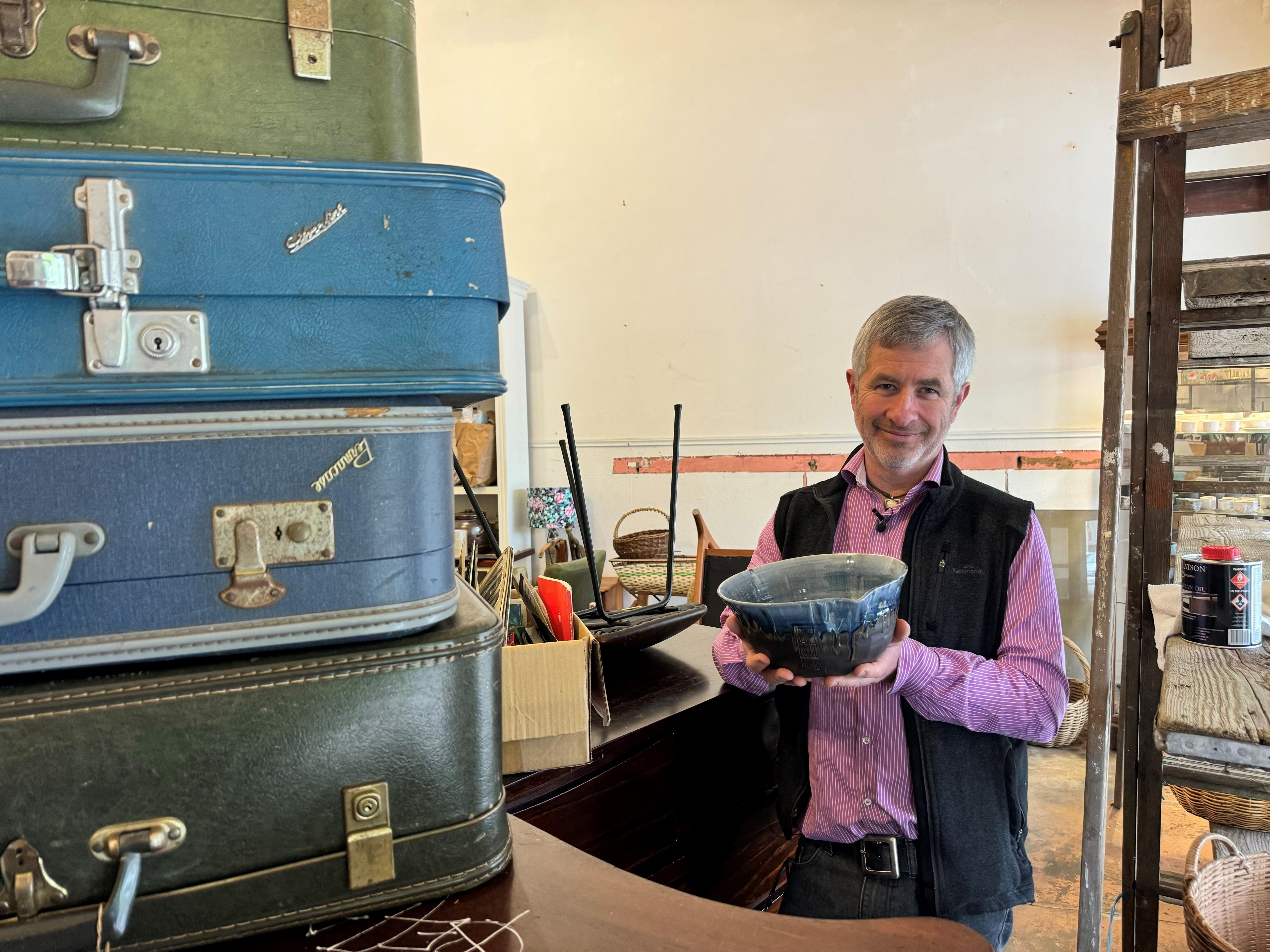 Tin Can Collective owner Tim Drylie holds blue coloured bowl behind table with drum casesinside store