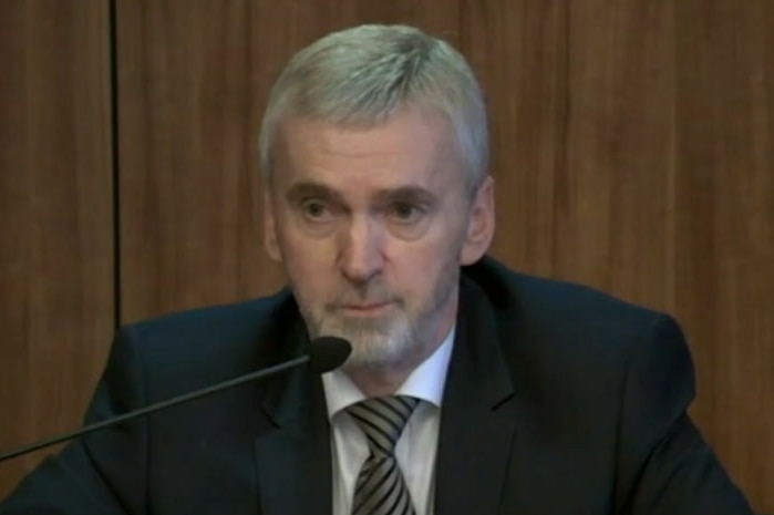 Ken Jones wears a suit with a grey and black striped tie as he sits in front of a microphone giving evidence to the commission.