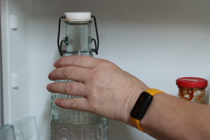 Hand reaching for a bottle of water on a fridge shelf.