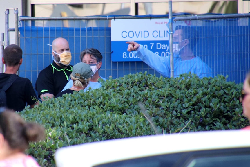 Doctors wearing full plastic shield face masks speak with people outside a COVID-19 fever clinic in Perth.