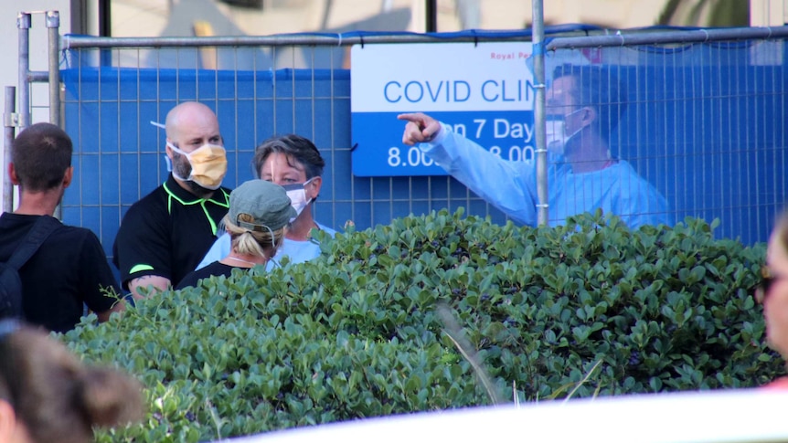 Doctors wearing full plastic shield face masks speak with people outside a COVID-19 fever clinic in Perth.