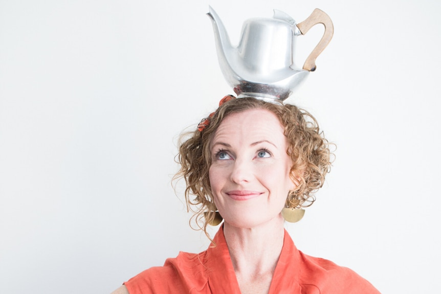 A white woman with curly hair has a silver teapot on her head.