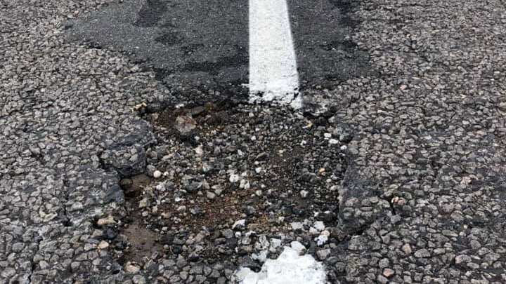 A hole in a road breaks up a freshly painted lane line.