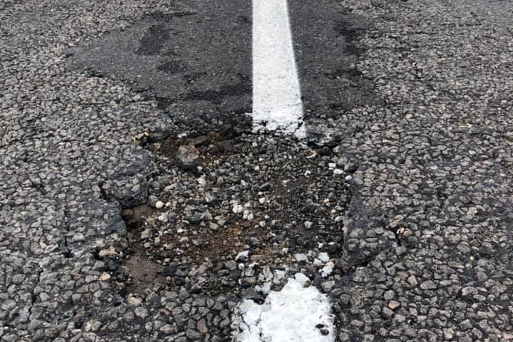 A hole in a road breaks up a freshly painted lane line.