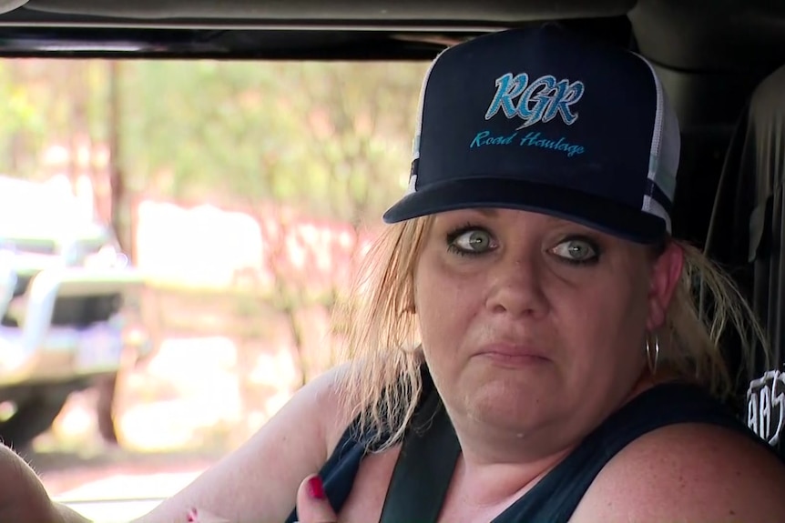 A blonde lady wears a cap and earings while seated in a truck