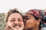 Man smiles at the camera while his girlfriend kisses him on the cheek, to depict talking about race in interracial relationships
