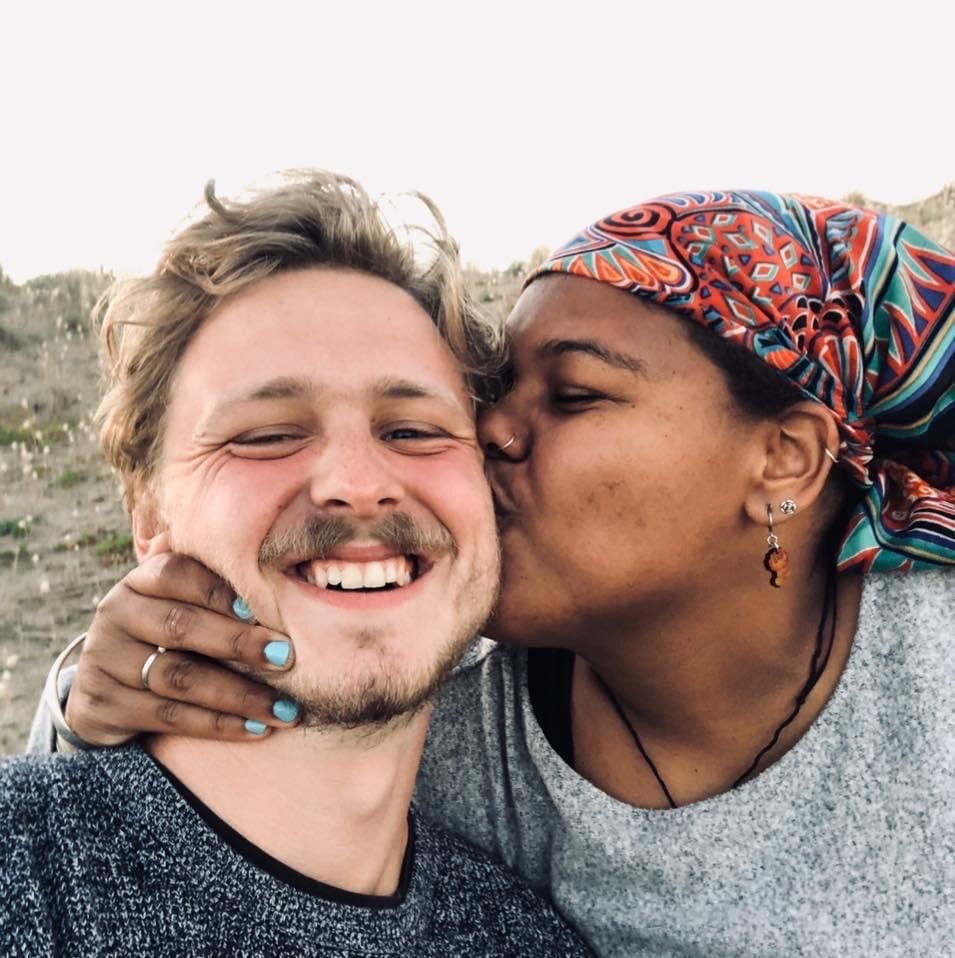 Man smiles at the camera while his girlfriend kisses him on the cheek, to depict talking about race in interracial relationships