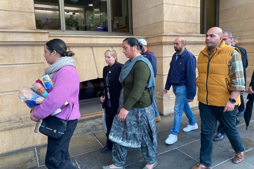 A woman in a dark green top and blue pants and skirt leaves court, surrounded by other people.